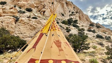 A tipi with a painted design, set against a rocky desert landscape.