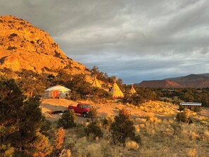 A desert landscape with a red pickup truck, a white tent, and several teepees.