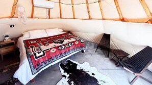 A cozy room with a bed, a chair, a small table, and a cowhide rug. - Native American Bison Tipi (Teasdale)