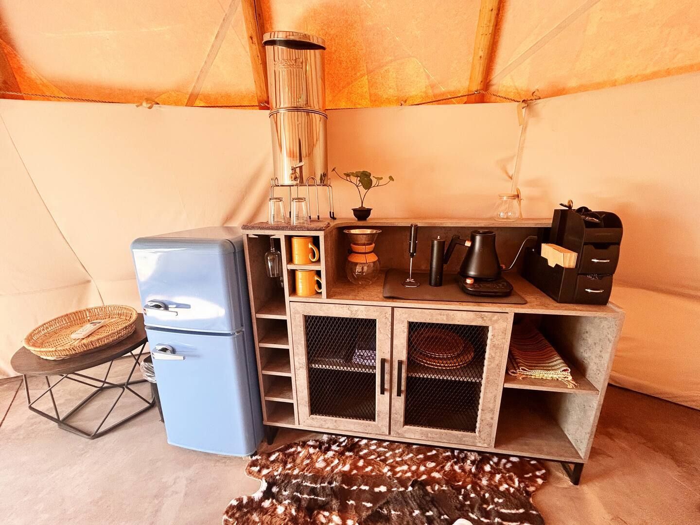 A compact kitchenette with a refrigerator, coffee maker, and storage cabinets.