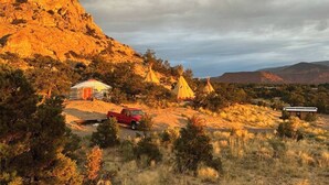 A desert landscape with a red pickup truck, a white tent, and several teepees. - Native American Bison Tipi (Teasdale)