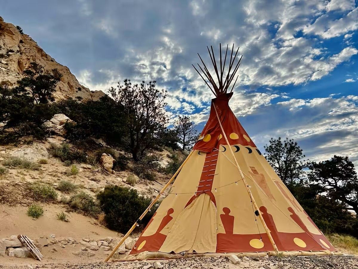Uma tipui tradicional com estrutura cónica e entrada circular, situada numa paisagem rochosa com vegetação escassa.