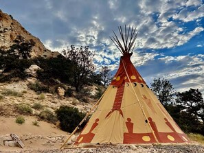 A traditional tipi with a conical structure and a circular entrance, set against a rocky landscape with sparse vegetation. - Glamping Tipi near Torrey and Capitol Reef (Teasdale)
