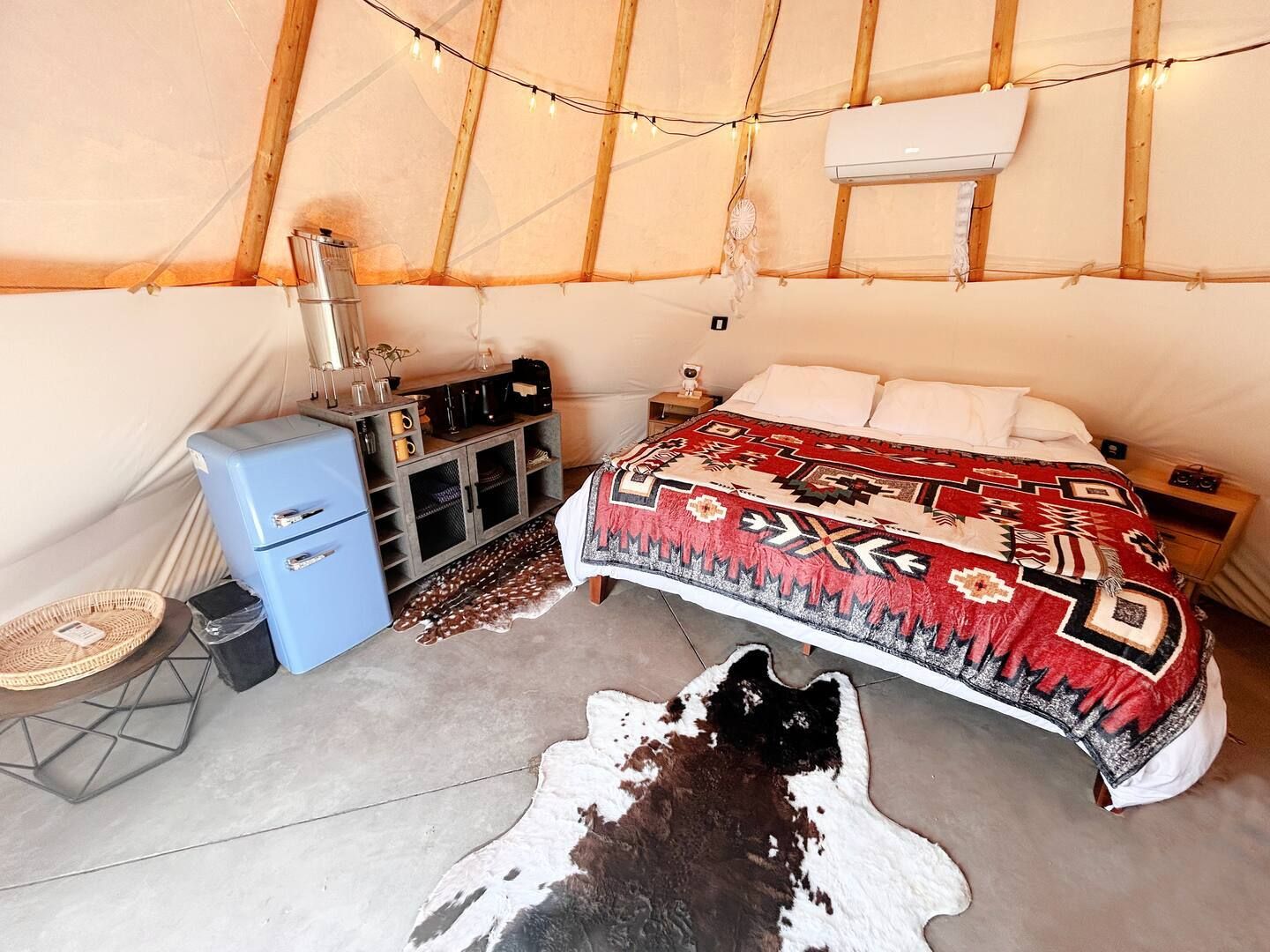 Um quarto aconchegante com uma cama, um pequeno armário azul, um aquecedor e um tapete de couro de vaca.
