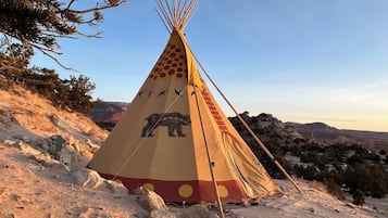 A traditional tipi with a bear design, set on a rocky hillside with a clear sky.