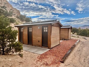 A rustic cabin with two wooden doors, a metal roof, and a gravel driveway. - Custom-built tipi, king bed, kitchenette, private bath (Teasdale)