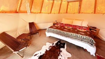 A cozy tent-style room with a bed, a chair, and a cow hide on the floor.