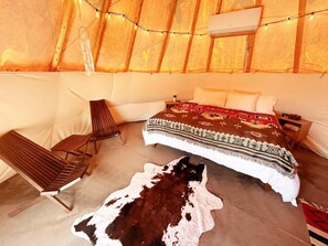 A cozy tent-style room with a bed, a chair, and a cow hide on the floor. - Custom-built tipi, king bed, kitchenette, private bath (Teasdale)