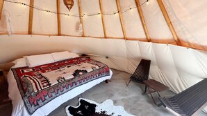 Een gezellig interieur van een tent met een bed, een stoel en een kluisvel rugtapijt.