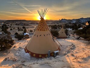 A snow-covered landscape with two tipi-style tents, one with a central pole and another with a decorative design. - Custom-built tipi, king bed, kitchenette, private bath (Teasdale)