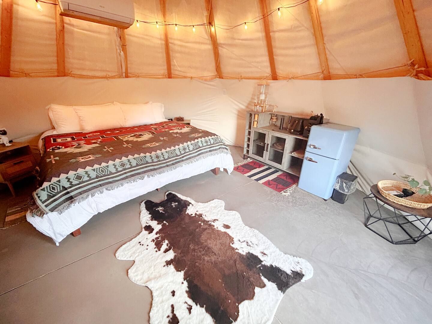 Een gezellige tentkamer met een bed, een klein kastje, een vachttapijt en sfeerverlichting.