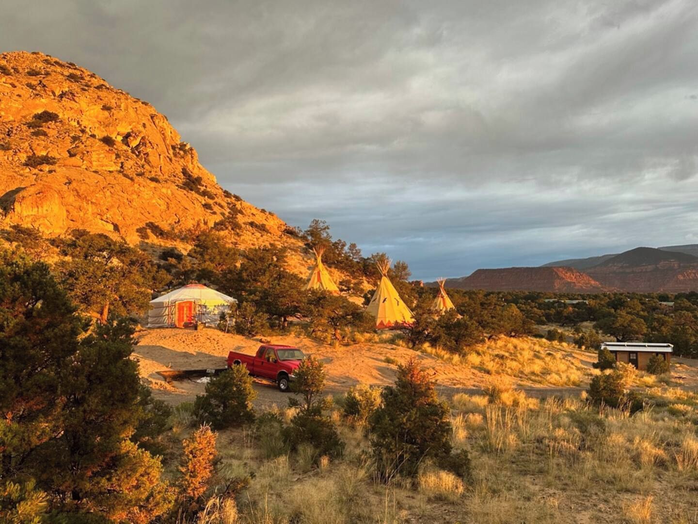 A desert landscape with a red pickup truck, a white tent, and several teepees.