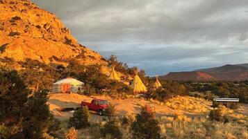 A desert landscape with a red pickup truck, a white tent, and several teepees.