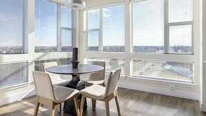 A modern dining area with a round table and four chairs, large windows with blinds, and a view of the cityscape. - Landing | Beautiful 2BD, Clubhouse, Gym (Denver)