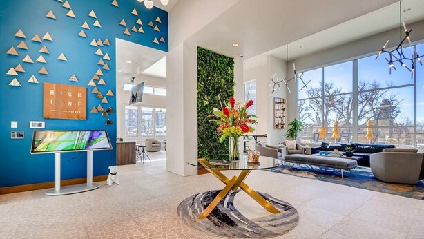 A modern lobby with a blue wall, a large TV, a reception desk, a sofa, and a decorative wall with greenery. - Landing | Beautiful 2BD, Clubhouse, Gym (Denver)