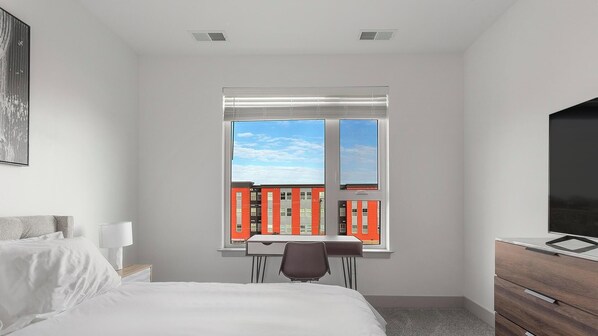 A bedroom with a bed, a desk, a chair, and a TV.