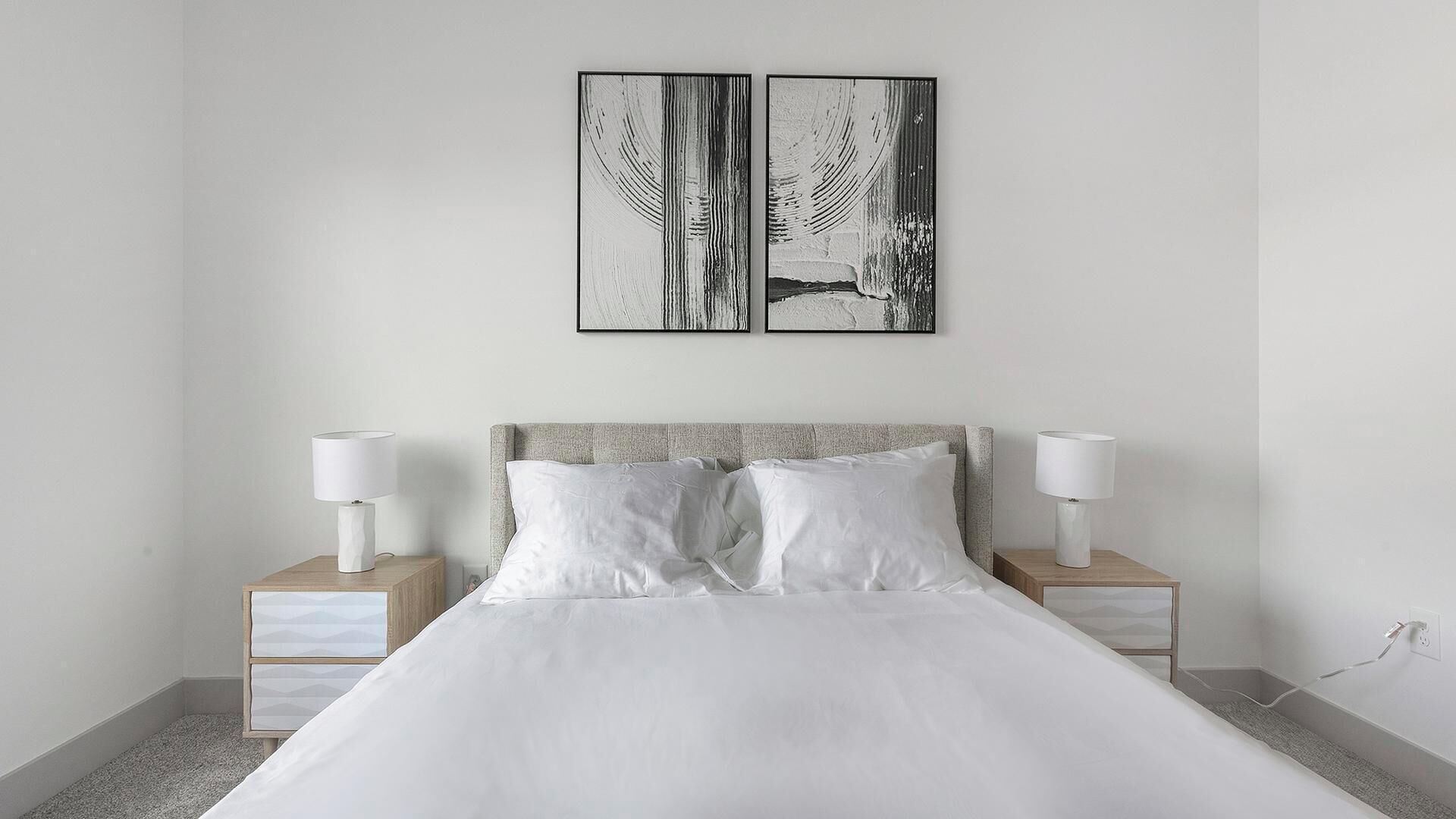 Quarto moderno com uma cama grande, duas mesinhas de cabeceira com luminárias e duas obras de arte em preto e branco na parede.