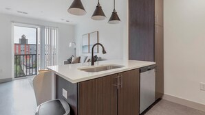 A modern kitchen with a white countertop, dark wooden cabinets, a built-in dishwasher, and pendant lighting. - Landing | Stylish 1BD, Gym, Clubhouse (Richmond)