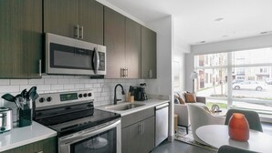 Une cuisine moderne dotée d’appareils électroménagers en acier inoxydable, d’un four à micro-ondes encastré et d’une grande fenêtre donnant sur la rue.