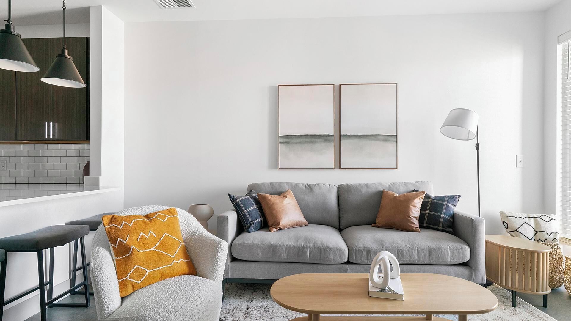 A modern living room with a grey sofa, a coffee table, and a kitchen area in the background.