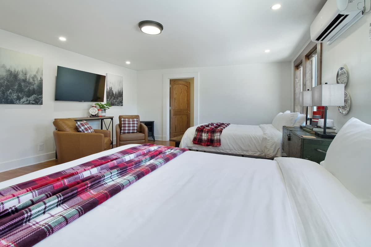 A modern hotel room with two beds, a flat-screen TV, a wooden door, and a small table with a lamp.