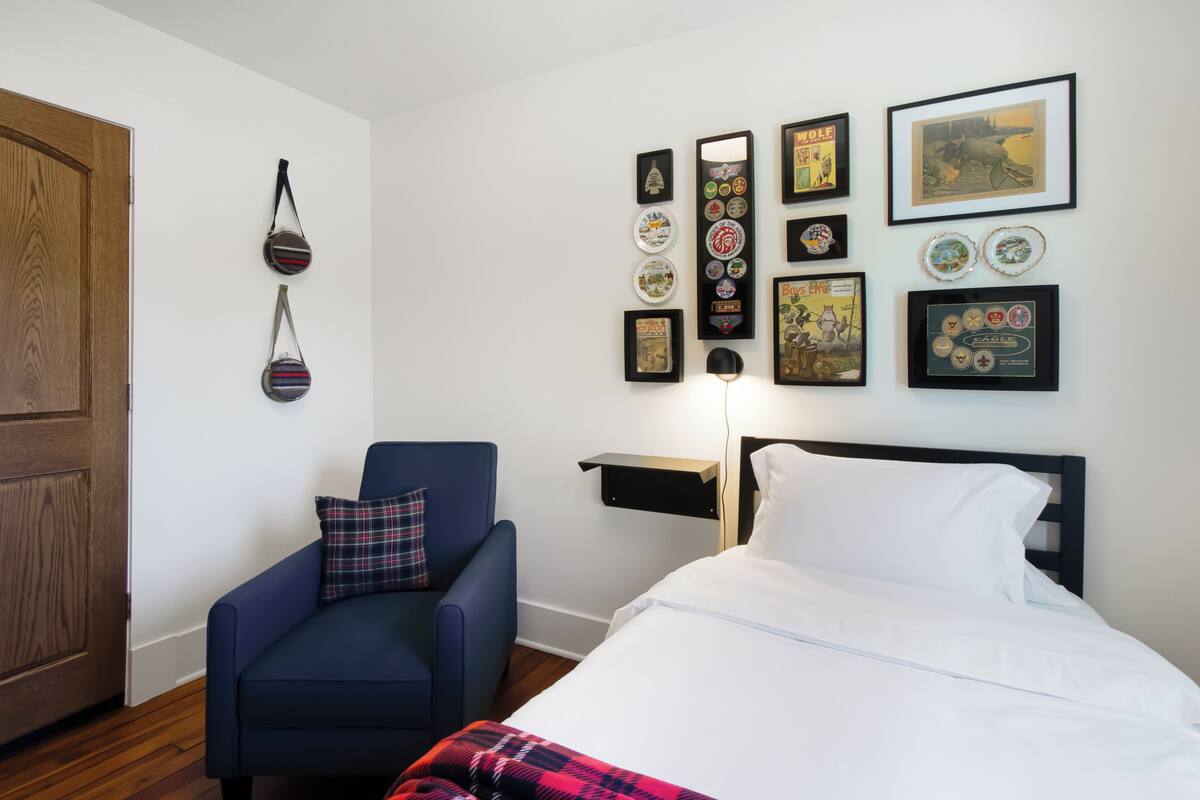 A hotel room with a bed, a blue armchair, a wooden door, and a wall adorned with various framed items.