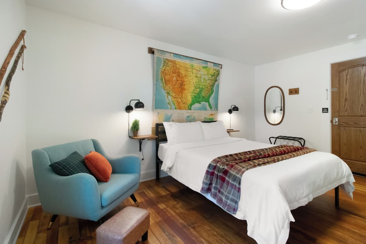 A bedroom with a bed, a blue armchair, a map on the wall, and a wooden floor.