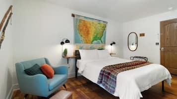 A bedroom with a bed, a blue armchair, a map on the wall, and a wooden floor.