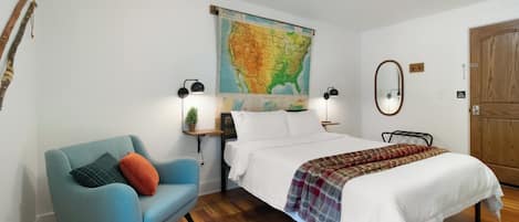 Un dormitorio con una cama, un sillón azul, un mapa en la pared y suelo de madera.