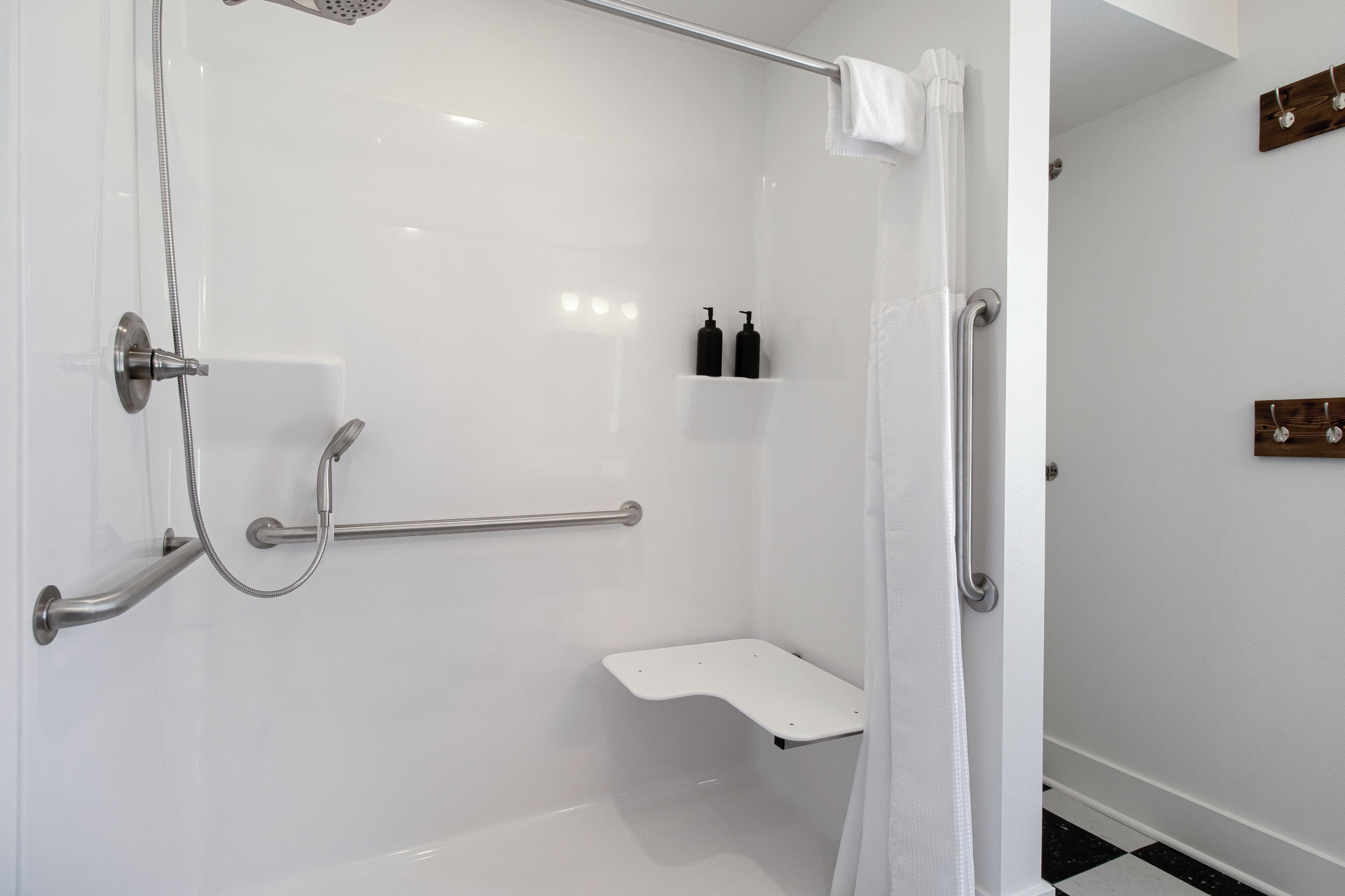 Un baño moderno con cabina de ducha, barras de apoyo, lavamanos blanco y perchero para toallas.