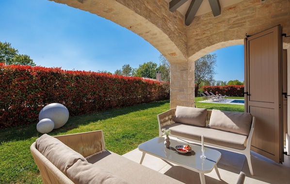 An outdoor seating area with a stone arch, a pool, and a hedge.