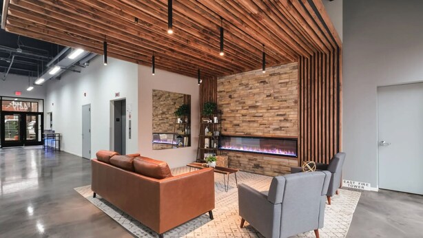 A modern lobby with a wooden ceiling, a fireplace, leather sofas, and a grey armchair. - Landing | Chic 2BD, Gym (Philadelphia)