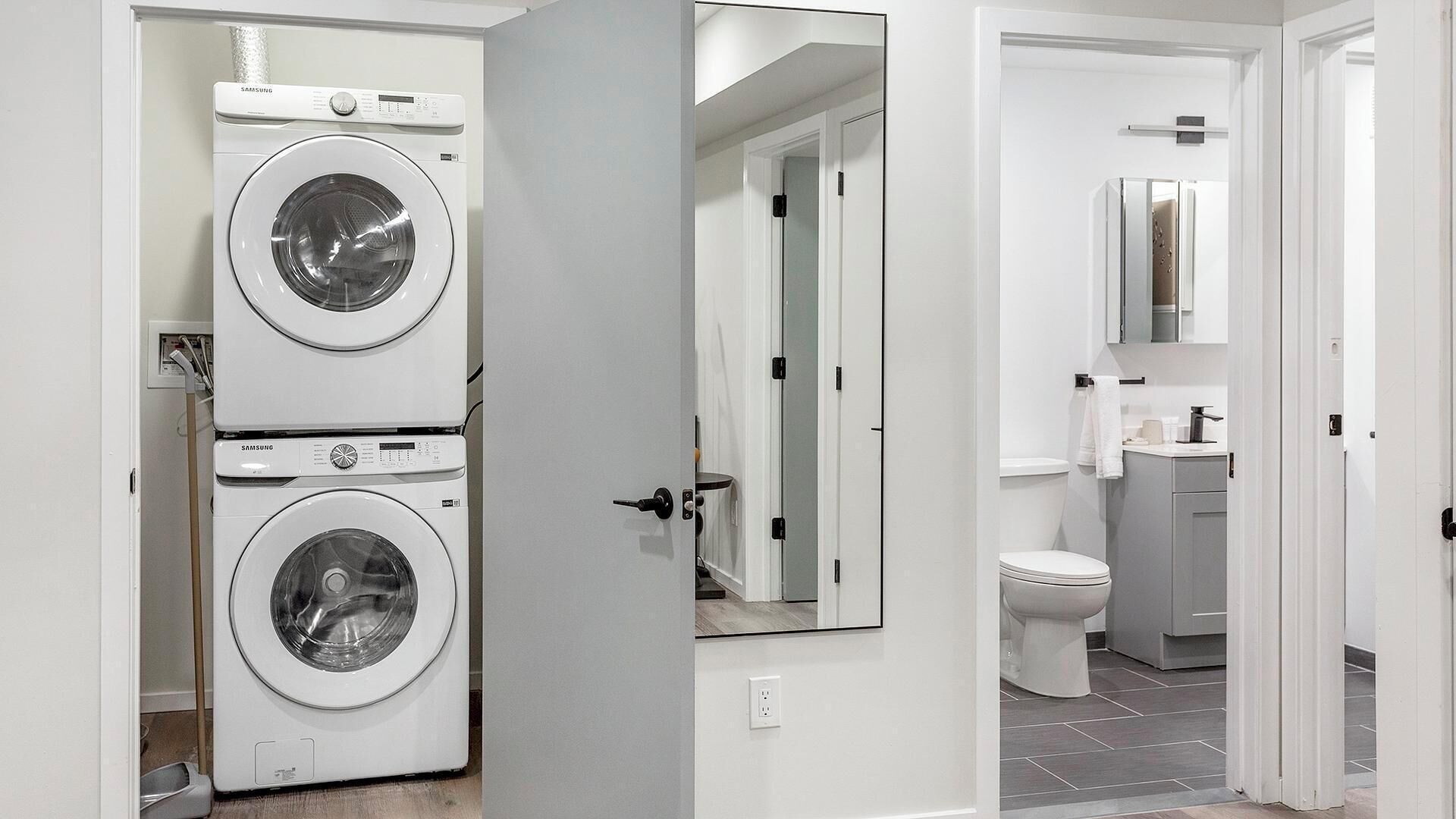 A laundry room with two stacked washing machines, a bathroom with a toilet and sink, and a mirror above the sink.