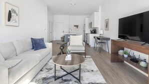 Ein modernes Wohnzimmer mit einer Couch, einem Couchtisch und einem Fernseher auf einem Holzgestell.