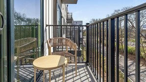 Ein Balkon mit Tisch und zwei Korbstühlen, mit Blick auf einen Parkplatz und Gebäude.