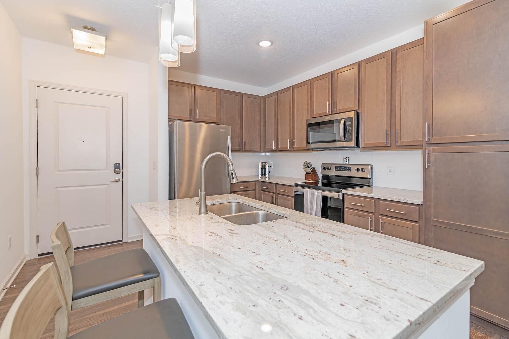A modern kitchen with wooden cabinets, stainless steel appliances, and a marble countertop.