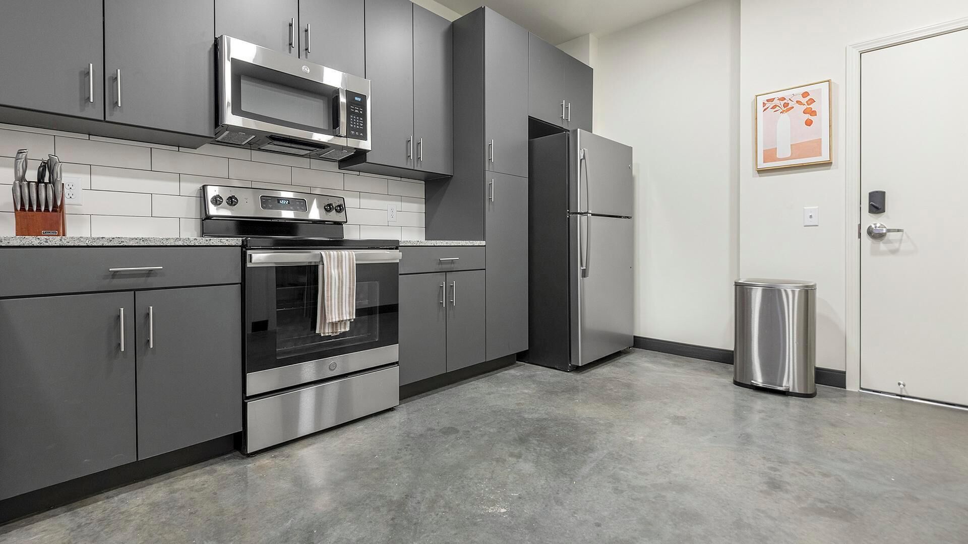 A modern kitchen with grey cabinets, a stainless steel microwave, oven, and refrigerator.