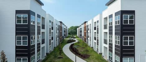 Un moderno complejo de apartamentos con un camino central, varios pisos y un diseño exterior uniforme.