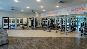 Un gimnasio amplio con máquinas de cardio, equipo de levantamiento de pesas y un muro con espejos.