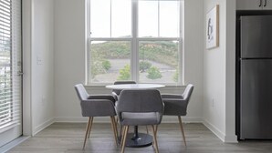 Una cocina con una mesa redonda y cuatro sillas, un ventanal con vistas a la vegetación y un refrigerador de acero inoxidable.
