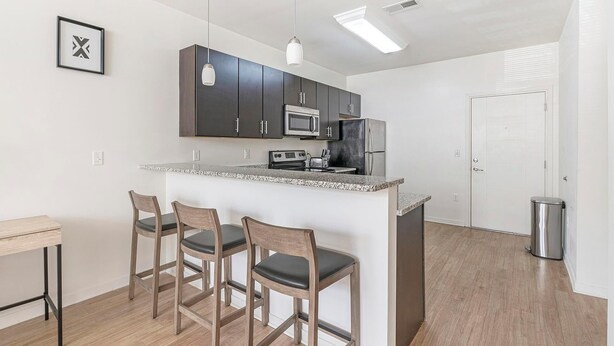 Una cocina moderna con armarios oscuros, una isla central con taburetes de bar, microondas, estufa y un cubo de basura.