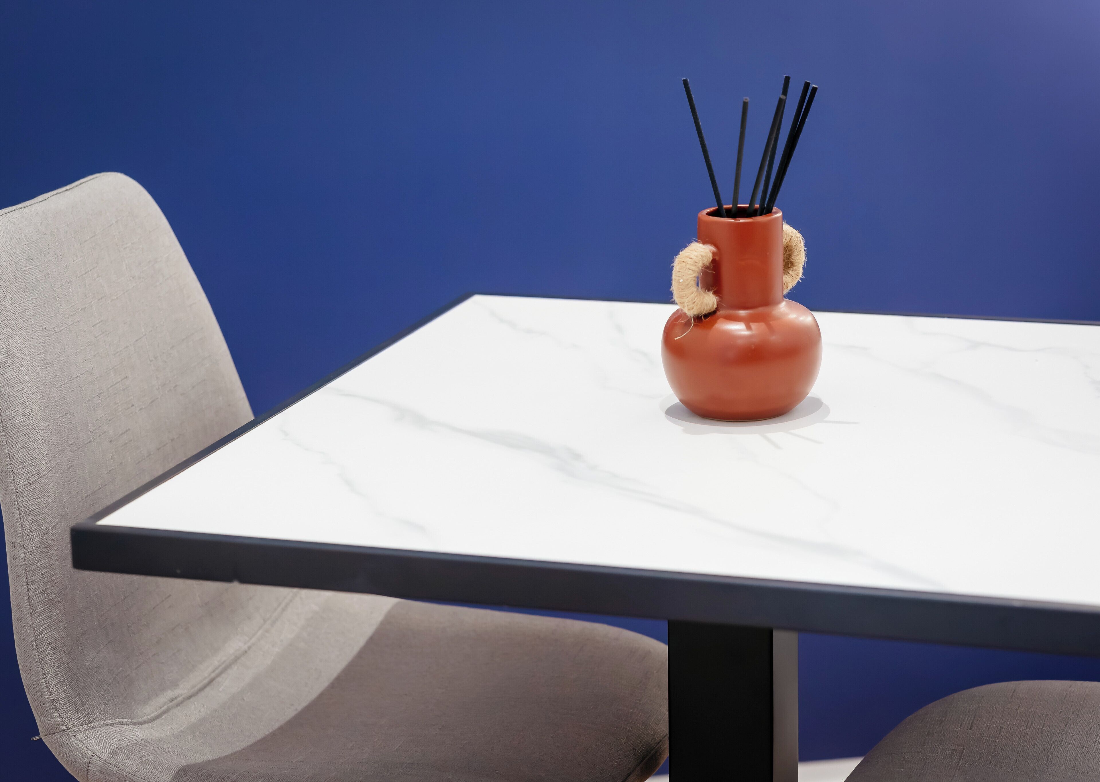 Une table sur laquelle se trouve un vase contenant des bâtonnets noirs, une chaise et un mur bleu.