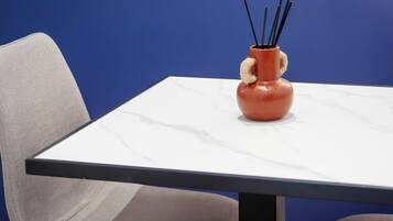 Une table sur laquelle se trouve un vase contenant des bâtonnets noirs, une chaise et un mur bleu.