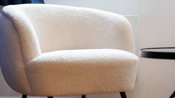 A white armchair with a textured fabric, positioned against a wall with a radiator and a dark curtain.