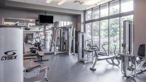 A gym with various exercise equipment, large windows, and a Cyrex machine. - Landing | Stunning 2BD, Courtyard, Pool (Hyattsville)