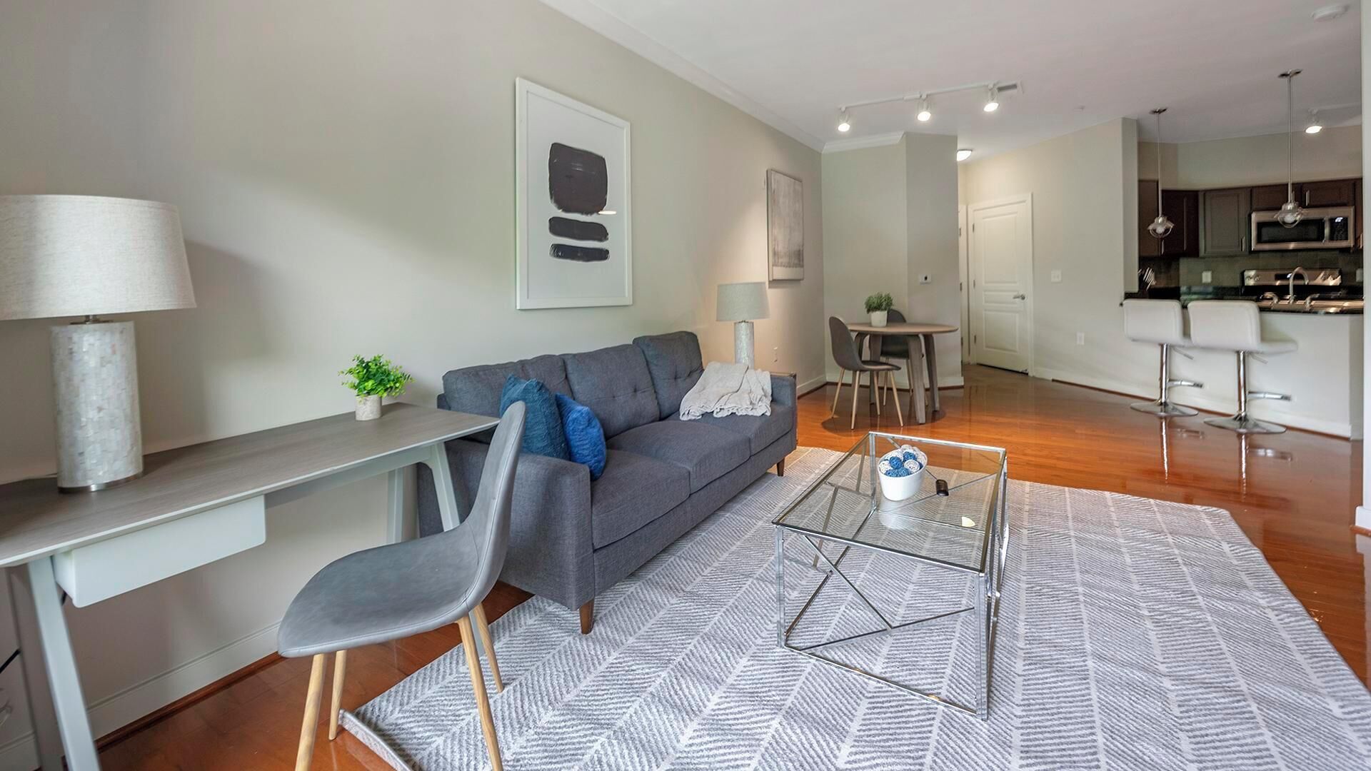 A modern living room with a grey sofa, a glass coffee table, and a dining area with a table and chairs.