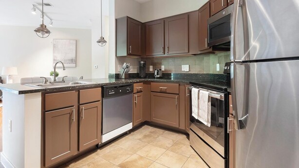 A modern kitchen with brown cabinets, stainless steel appliances, and a tiled backsplash.