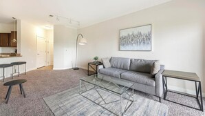 A modern living room with a grey sofa, a glass coffee table, and a minimalist design. - Landing | Stylish 1BD, Clubhouse, Courtyard (Hyattsville)