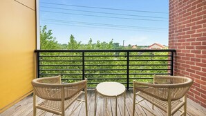 A balcony with two wicker chairs and a small round table, overlooking a green landscape with trees and a building labeled "The Home Depot". - Landing | Stylish 1BD, Clubhouse, Courtyard (Hyattsville)