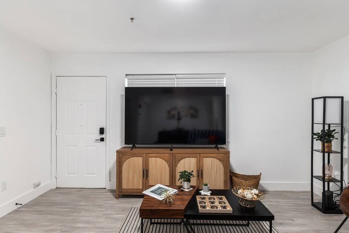 Una sala de estar con una amplia televisión de pantalla plana, armarios de madera, una mesa de centro y una estantería.